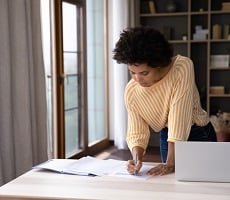 person using a computer and writing in a notebook