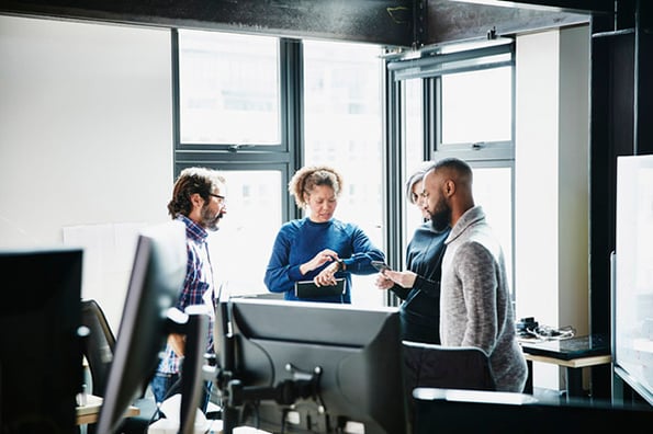 Mitarbeitende stehen in Büro und besprechen Aufgaben priorisieren 