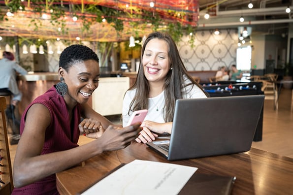 Lachende Frauen vor Laptop nutzen dApps auf Smartphone