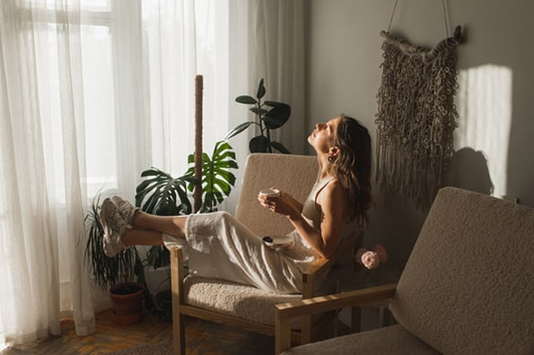 Entspannte Frau vor Fenster zuhause genießt Digital Detox