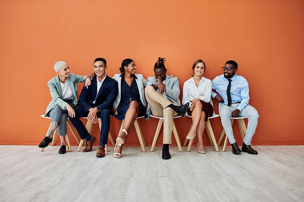 Sechs Mitarbeitende auf Stühlen vor orangenem Hintergrund freuen sich über gelungenes Employer Branding