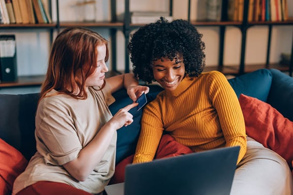 Zwei Frauen beim Google Shopping auf Sofa vor Laptop