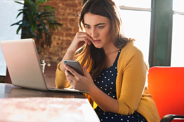 Besorgte Frau vor Laptop sitzend, sucht nach IP-Adresse am Smartphone