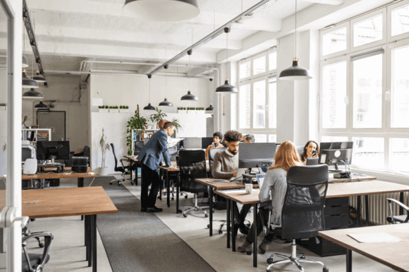 Office Manager steht an Tisch und unterhält sich mit Mitarbeitenden im Büro