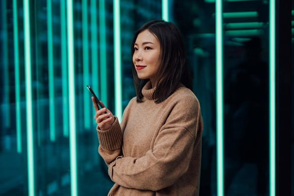 Frau mit Smartphone in Hand vor Wand mit leuchtenden Balken denkt an Web 3.0