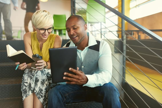 Two creative millenial small business owners working on social media strategy using a digital tablet while sitting in staircase-3