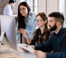 three people talking around a computer in an office