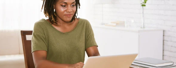 Marketer, wearing a green short sleeve shirt, sits at a desk typing on a computer to build a company profile.