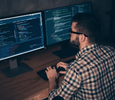 person writing code on two computer monitors