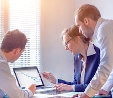 three people using a laptop in an office