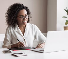 person using a laptop and writing on a notepad