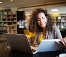 person using a computer and reading a notebook in a library