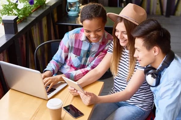 three gen-z people smiling while looking at laptop and tablet