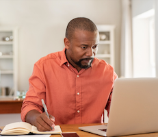 man using a laptop and writing notes