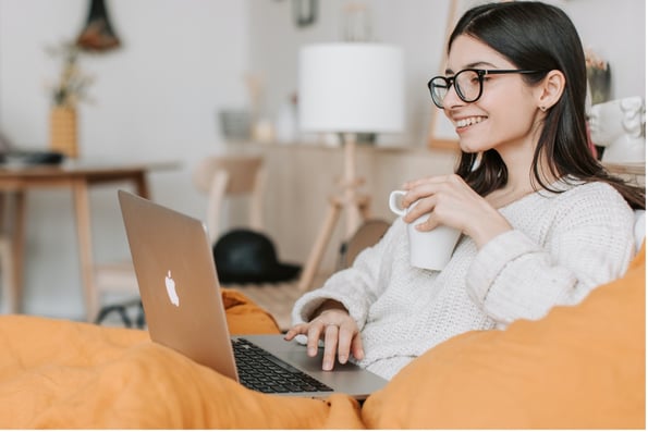 jeune femme buvant un café sur son canapé devant son ordinateur