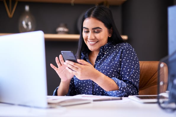 mulher cria lista de transmissão no WhatsApp usando telefone celular e lendo instruções no computador à sua frente