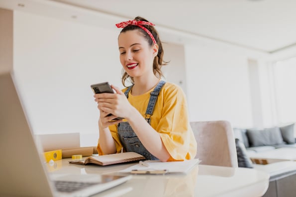 mulher sentada em frente a um computador mexe no celular, aprendendo como usar a automação no Instagram 