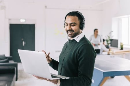 A project manager monitors a project from his laptop while wearing headphones