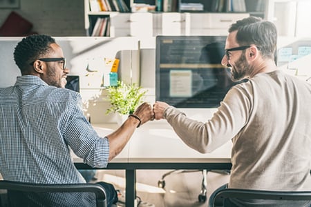 Loyal customer fist bumping a customer service representative in an office setting to celebrate a referral customer