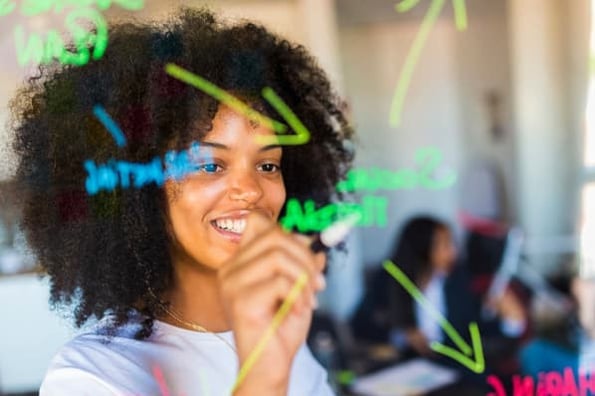 A woman writes content marketing statistics and trends on a clear board with marker.