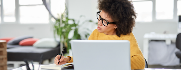 person using a laptop in an office and writing notes