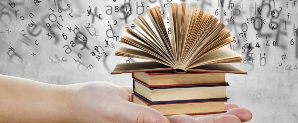 hand holding books with letters and numbers floating above it