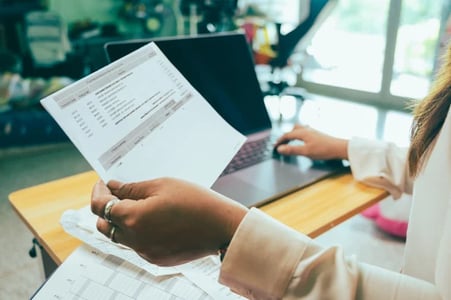 person holding an invoice in one hand and typing with the other